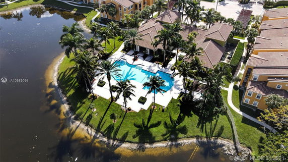Aerial view of a residential area with a central building next to a lake, surrounded by trees and pathways.