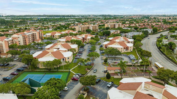 Aerial view of a residential complex with multiple buildings, parking areas, and a tennis court.