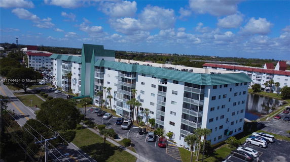 Front view of a multi-story residential building with green roofs and parking area.