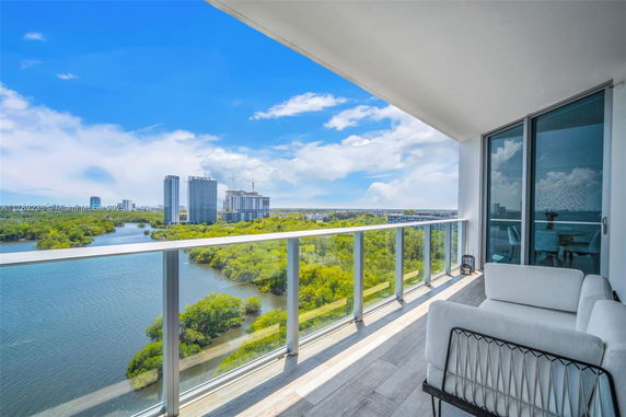 Balcony with glass railing overlooking a river and city buildings.