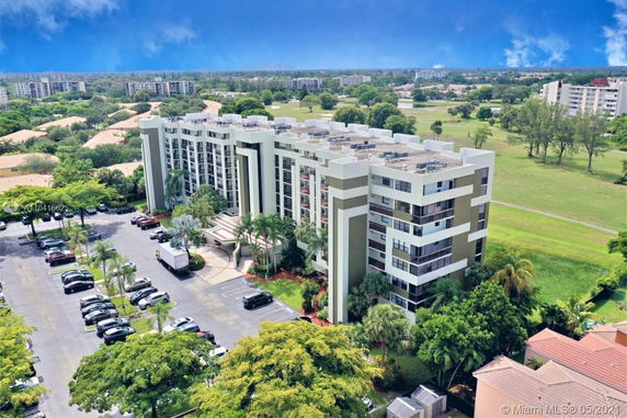 Aerial view of a multi-story building with parking lot and green landscape in the background.