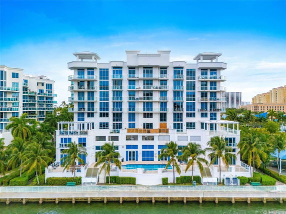 Front view of a multi-story modern apartment building with numerous balconies beside a body of water.