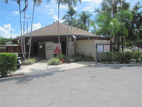 Front view of a small building with a sloped roof and entrance surrounded by palm trees.