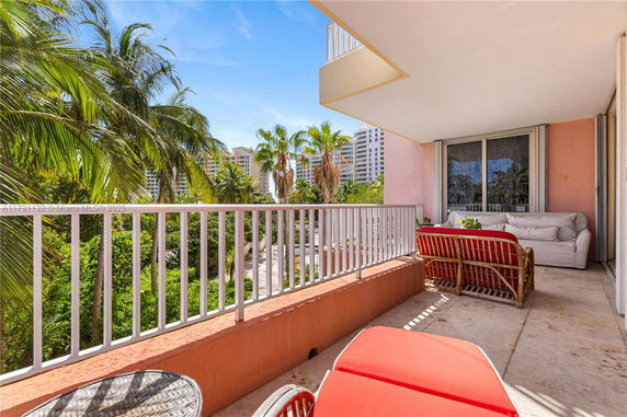 Balcony view with seating and railing, overlooking palm trees and distant high-rise buildings.