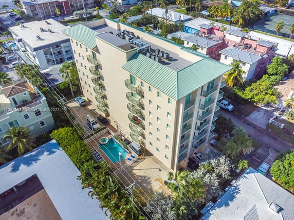 Aerial view of a multi-story building with a green roof and a rooftop featuring air conditioning units. The building has balconies and a swimming pool at the ground level.