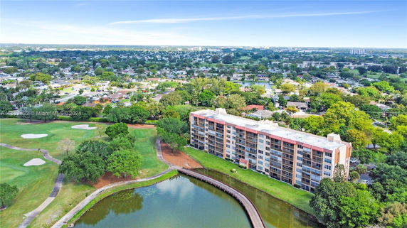 Aerial view of a multi-story building adjacent to a golf course and surrounded by residential areas.