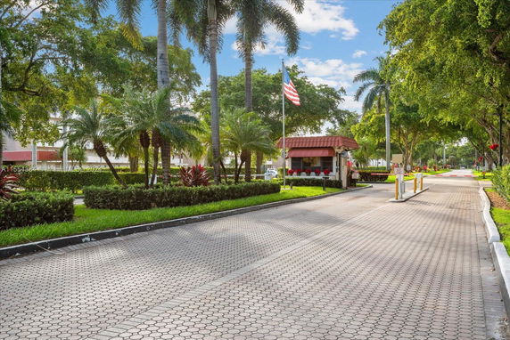 Entrance area with a security booth and palm trees.