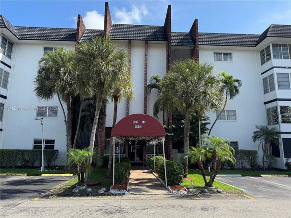 Front view of a three-story building with palm trees and a red awning at the entrance.