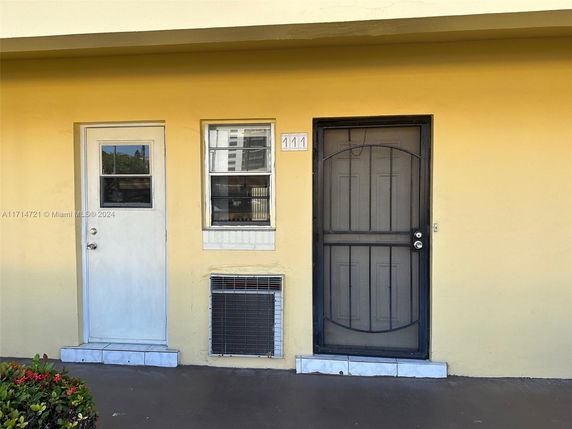 Front view of a building with a yellow exterior, featuring one door and one window.