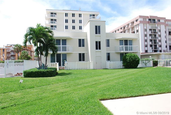 Front view of a multi-story residential building with balconies and a surrounding white fence.
