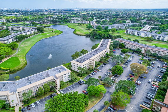 Aerial view of several buildings near a lake with ample greenery and parking areas around.
