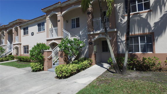 Front view of a two-story residential building with white railings and arched entryways.