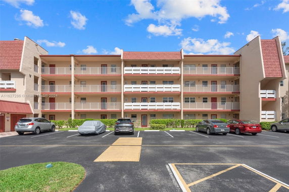 Front view of a multi-story apartment building with balconies and parking area.