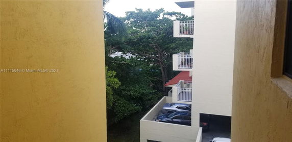 View of building with balconies and surrounding trees, seen from another building.
