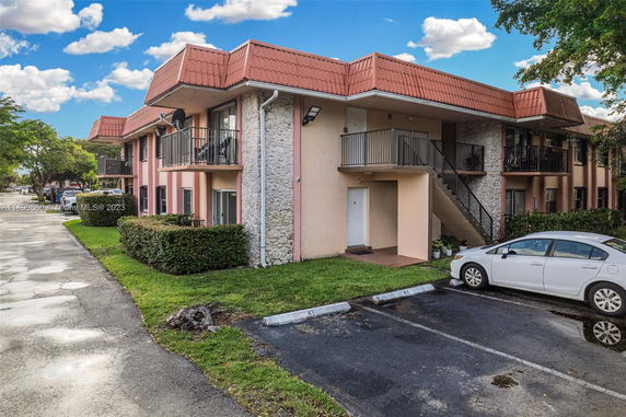 Front view of a two-story residential building with balconies and a parking area in front.