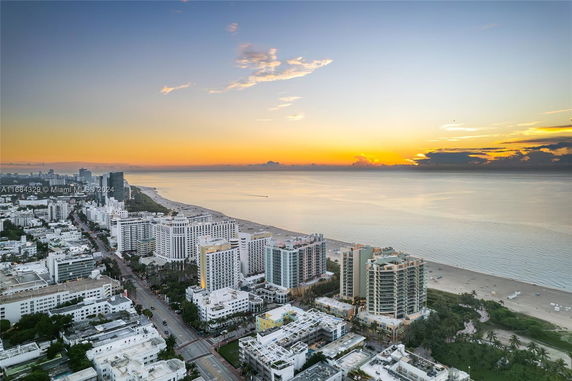Panoramic view of a coastal cityscape with high-rise buildings along the shoreline at sunrise.