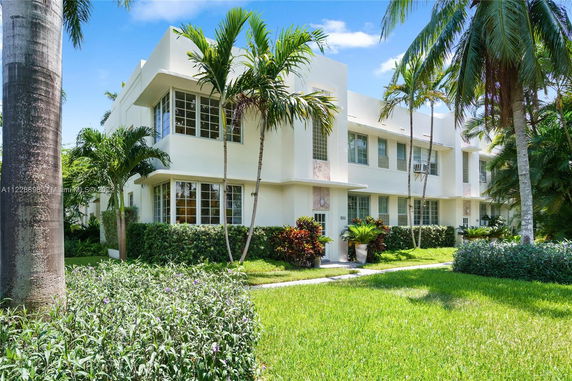 Front view of a two-story building with large windows and tropical plants.