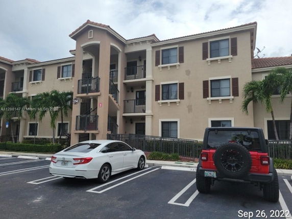 Front view of a three-story building with balconies and parking area.