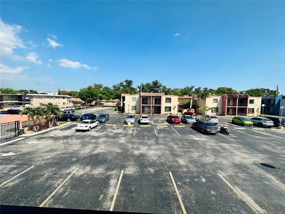 Outdoor parking area with multiple vehicles and residential buildings in the background.