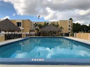 Outdoor swimming pool with an adjacent building and thatched roof structures.