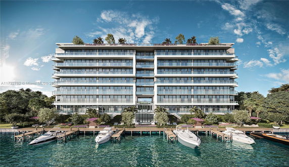 Front view of a modern multi-story building with balconies and rooftop greenery, situated by a waterfront with boats docked.