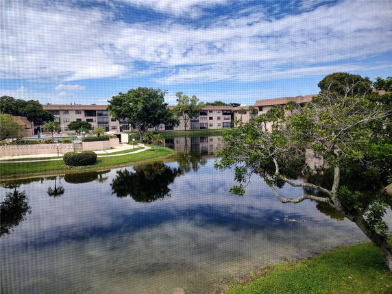 View of residential buildings across a pond with trees and a clear blue sky.