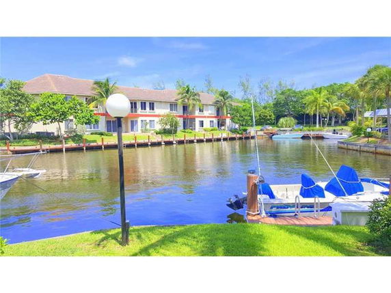 View of a canal-side building with boats docked nearby, surrounded by trees and water.