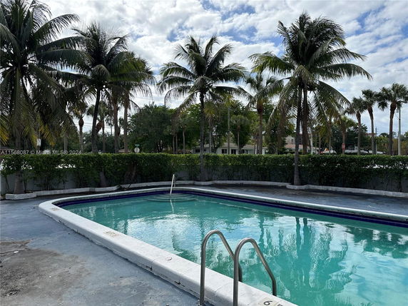 Outdoor swimming pool with palm trees in the background.