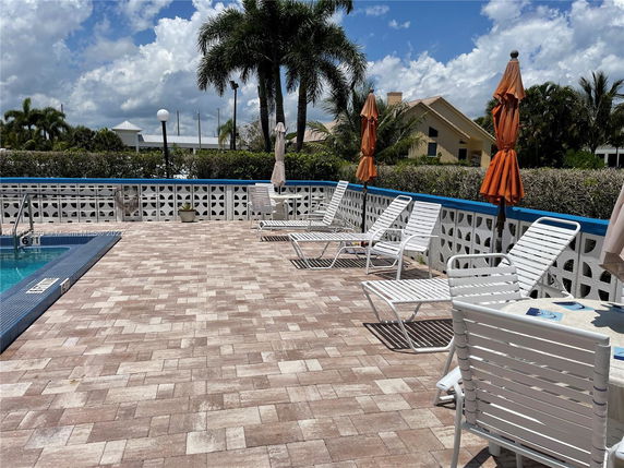 Outdoor poolside area with lounge chairs and umbrellas, adjacent to a light-colored house.