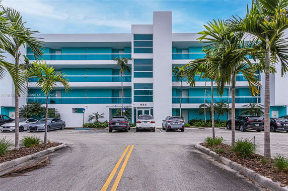 Front view of a multi-story building with turquoise accents and a parking area in front.