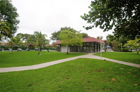 View of a single-story building with a red roof surrounded by grass and trees.