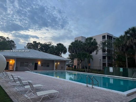 An outdoor swimming pool area with several lounge chairs and a building in the background.