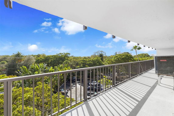 View from a balcony overlooking a parking area and trees.