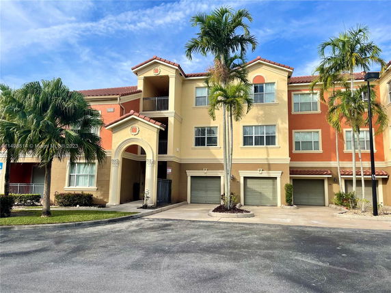 Front view of a multi-story apartment building with multiple garages and an arched entrance.