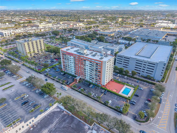Aerial view of a multi-story residential building with surrounding parking areas and nearby structures.