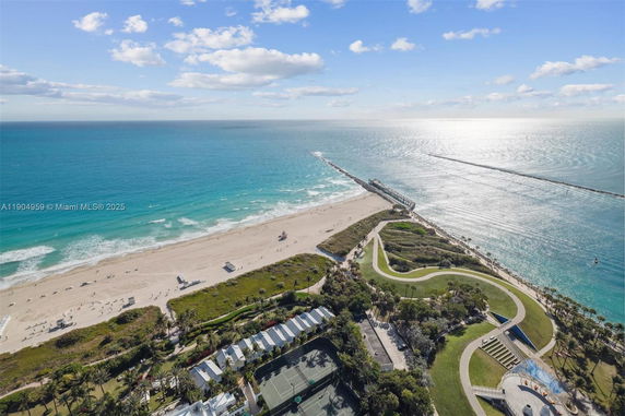 Wide angle view of a beach and ocean with adjacent green areas and pathways.