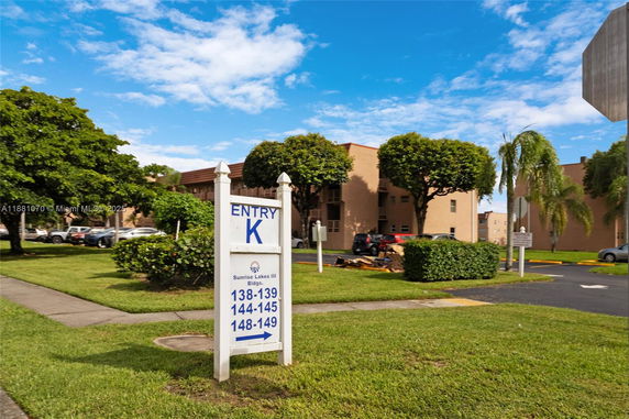 Front view of a multi-story residential building with an entry sign and landscaped surroundings.