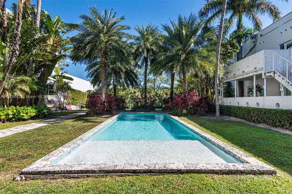 Outdoor view of a swimming pool surrounded by palm trees and a white two-story building.