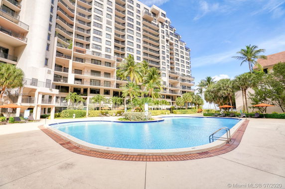 Front view of a multi-story residential building with balconies and a swimming pool in front.