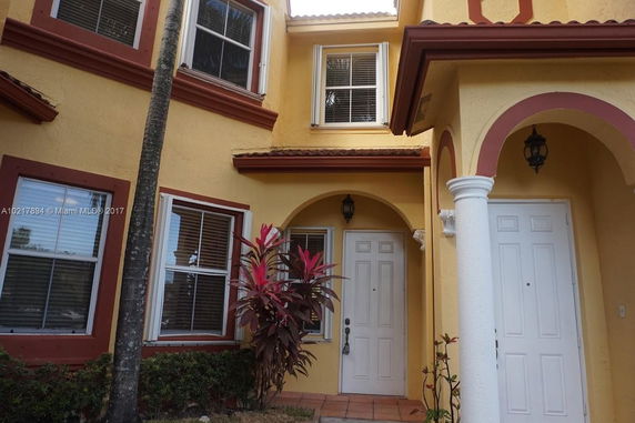 Front view of a yellow two-story house with white doors and decorative arches.