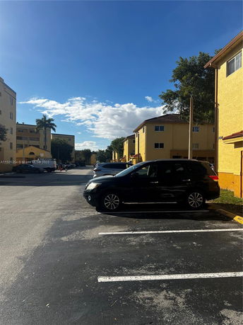 Outdoor parking area with several cars parked next to yellow residential buildings.