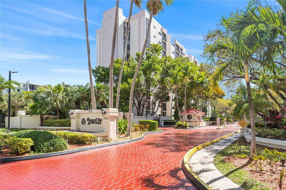 Front view of a multi-story residential building with a red brick driveway and palm trees.