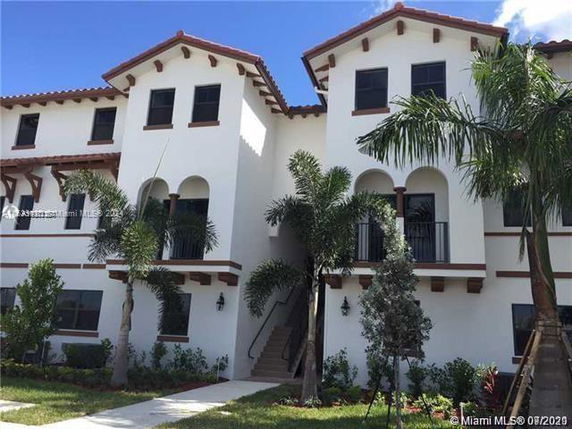 Front view of a three-story residential building with arched windows and palm trees.