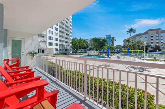 View from a balcony overlooking an outdoor swimming pool area and surrounding buildings.