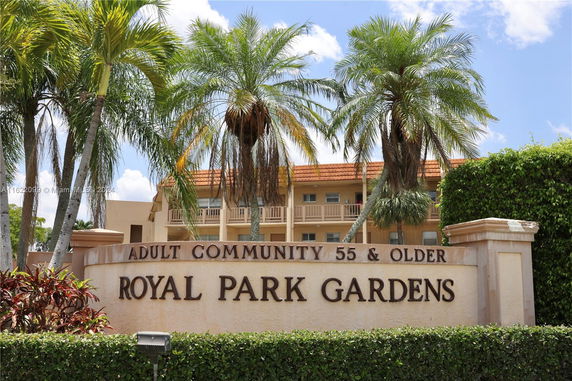 Front view of a residential building in an adult community with palm trees and a sign for Royal Park Gardens.