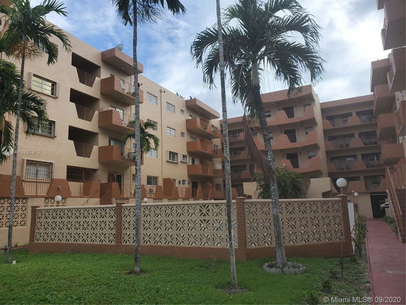 Front view of a multi-story apartment building with balconies and a decorative fence.