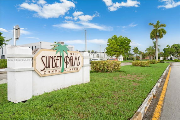 Front view of a condominium sign with 'Sunset Palms' and a partial view of the building in the background.