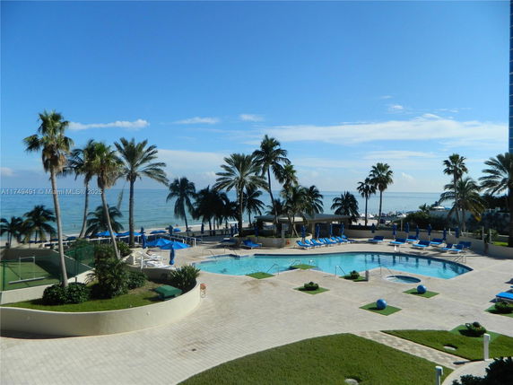 Outdoor swimming pool area overlooking a beach with palm trees and seating.