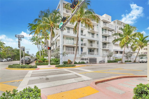 Front view of a multi-story residential building with balconies and palm trees.