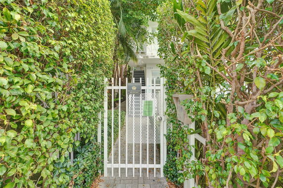 Front view of a house with a white metal gate and dense greenery.